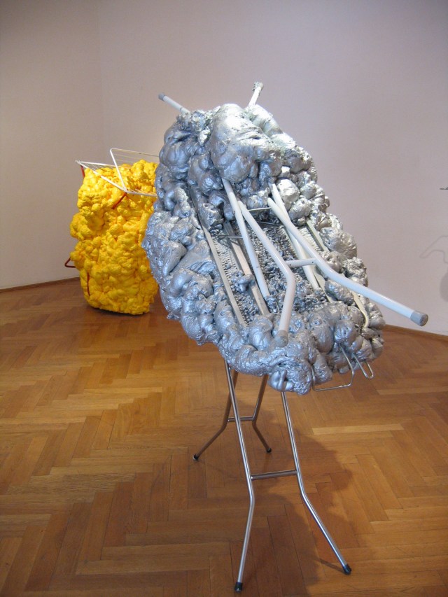 © Wilhelm Roseneder. Silberne Erweiterung/Silver expansion, 2006/2007. Austrian Cultural Forum. Bratislava, Slovakia 2007.  Bügelbrett, Styropor, Plastikflaschen, Klebeband, Verpackungsmaterial, Polyurethan, Lack/Ironing board, styropor, plastic bottles, sticky tape, packing materials, polyurethane, varnish, 1.40x1.50x90 cm. Gelbe Erweiterung/Yellow expansion, 2006/2007. Wäschetrockner, Styropor, Plastikflaschen, Klebeband, Verpackungsmaterial, Polyurethan, Lack/Airiel drier, styropor, plastic bottles, sticky tape, packing materials, polyurethane, varnish, 1.26x1.23x90 cm